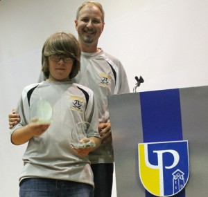 Student José Poskauer (front) holds up his first-place win earned during this weekend's Mathcounts competition. His father Tim Proskauer stands behind him.