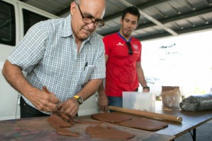 Professor Jaime Suárez, takes the shape of the hands of the kids, staff and partners of the Center to create a ceramic mural, as Olympian Tommy Ramos (right) looks on.