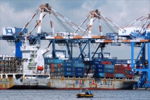Men in a small tugboat row past the giant Singapore-registered Wan Hai 225 cargo ship as its containers are unloaded by cranes at Taiwan’s southern port of Kaohsiung. (Credit: Larry Luxner)